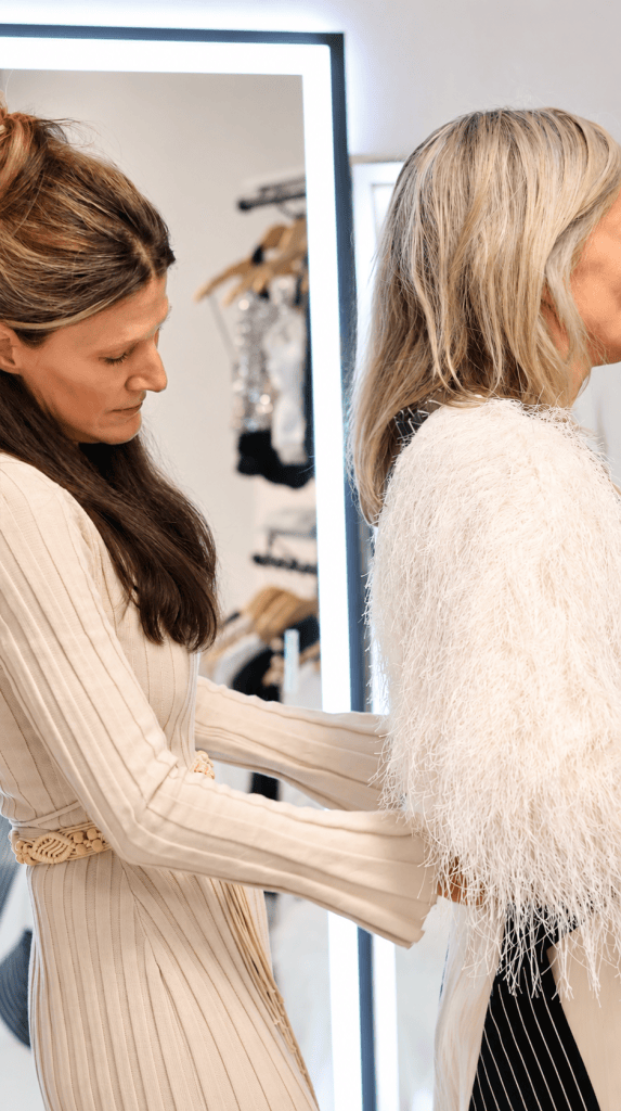 Stylist helping a client try on a feathered cream jacket in front of a mirror during a Denver personal styling session